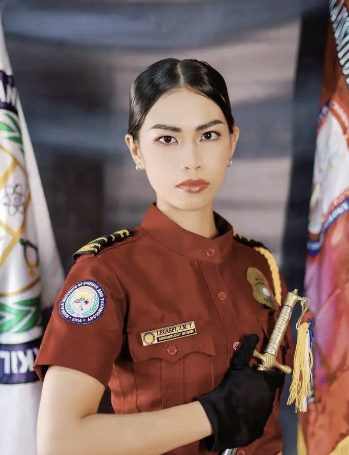 Joana Marie Legaspi in her maroon criminology intern uniform, standing between flags