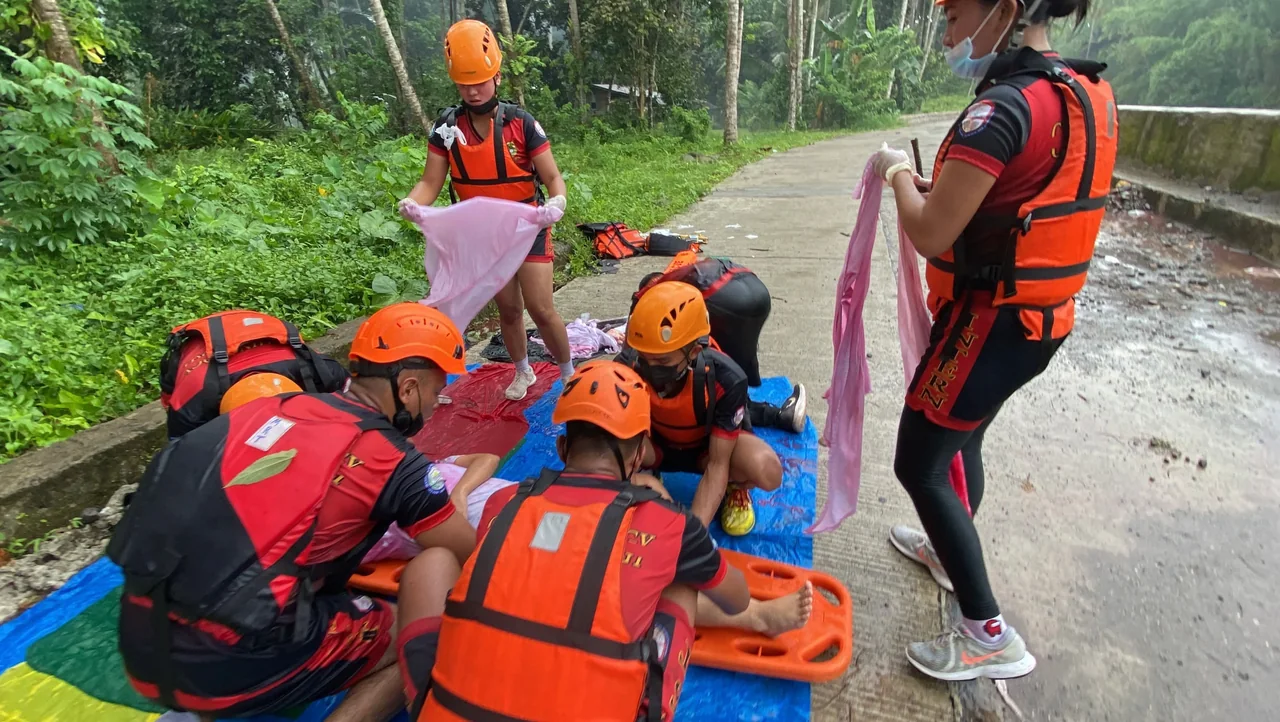 Trainees practising bandaging and casualty handling around a person on a spine board beside a river
